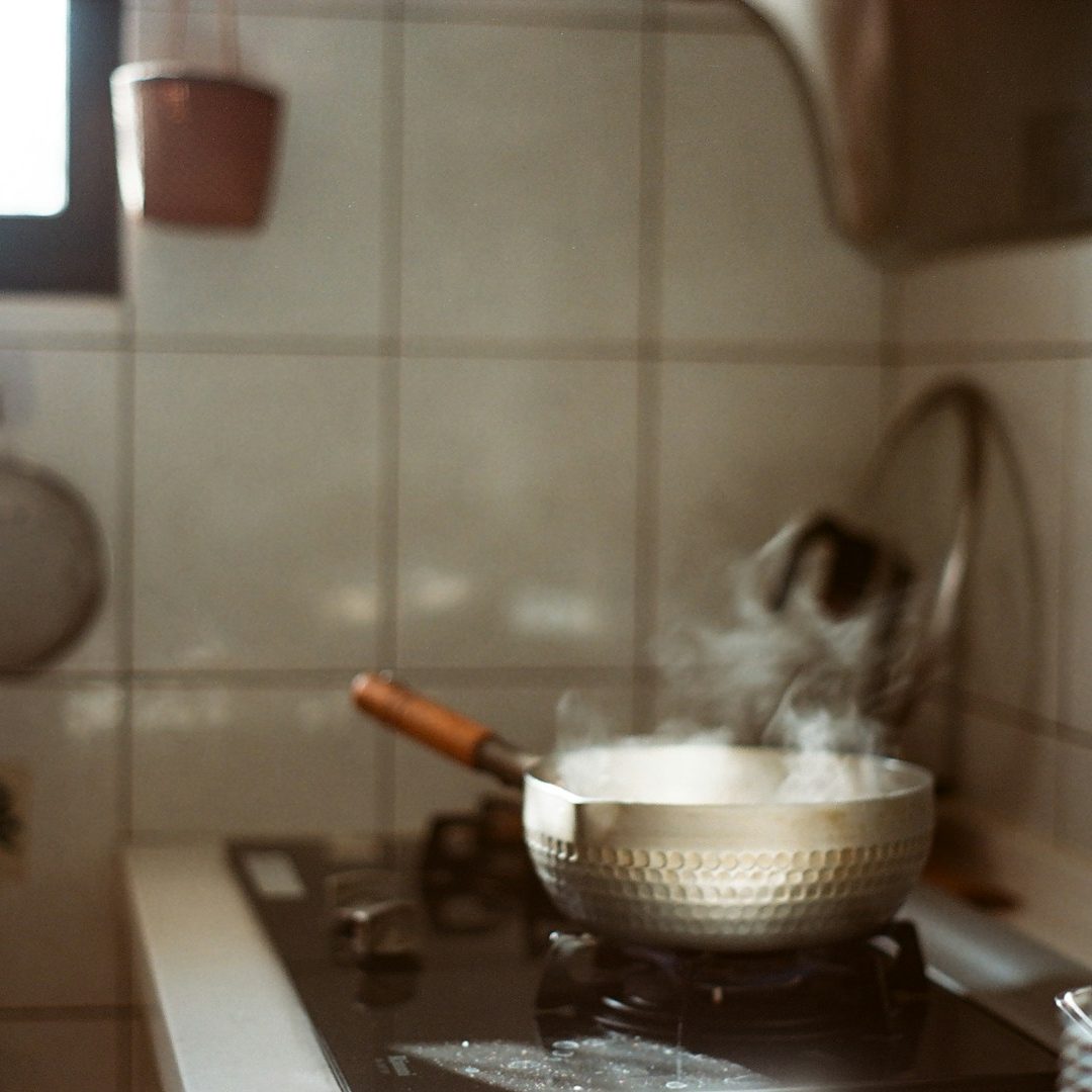 Olla humeante sobre una cocina con azulejos claros y utensilios al fondo.